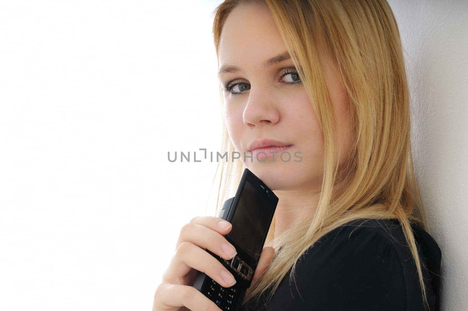 Blond thoughtful young woman holding mobile phone on white background