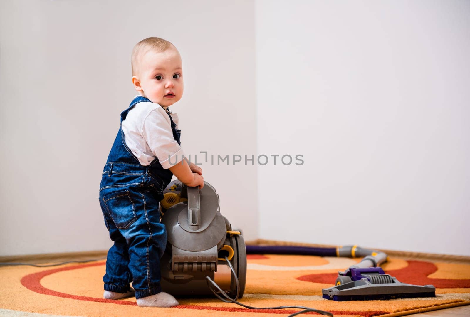 Little baby standing at vacuum cleaner - home interior