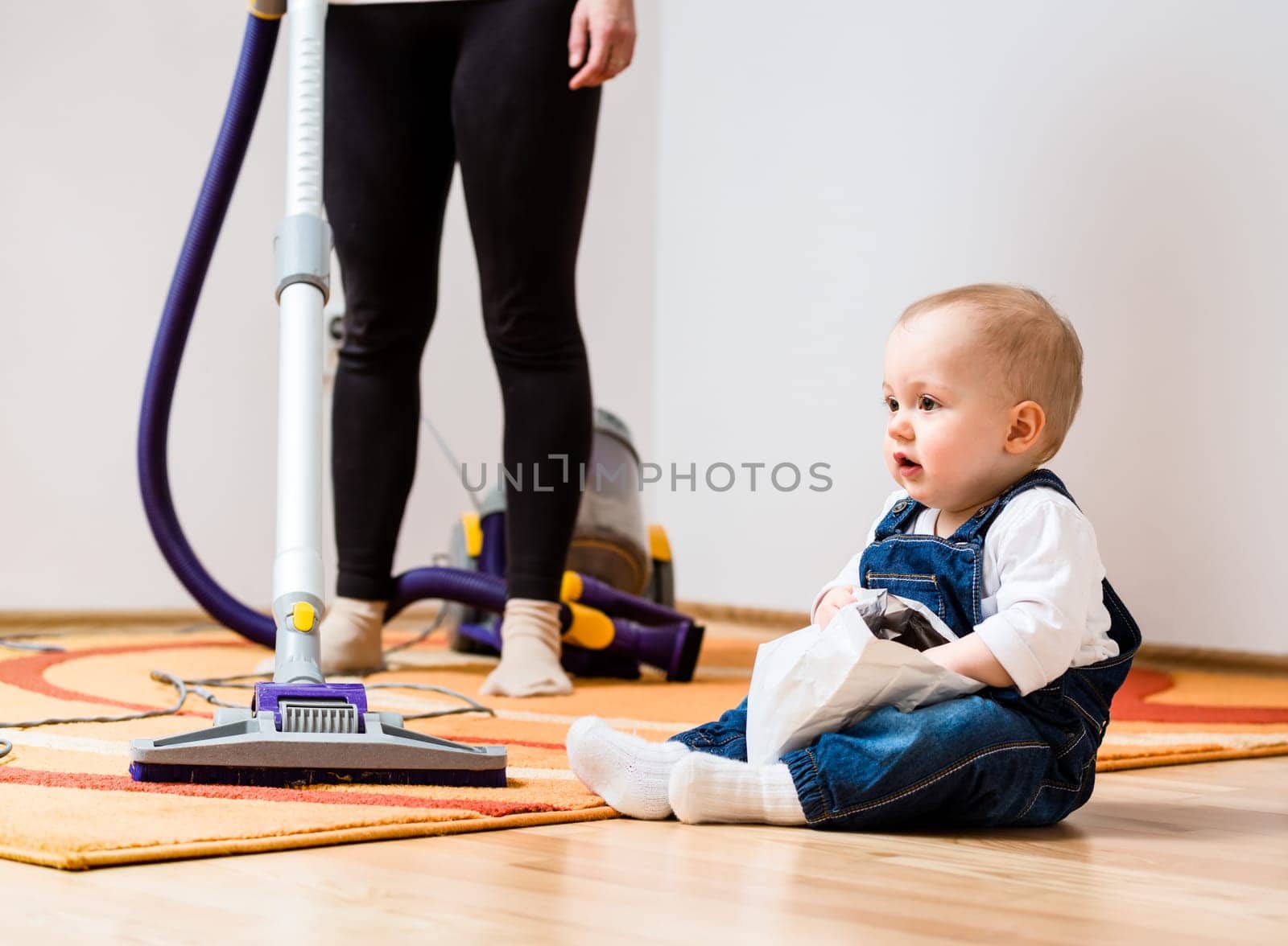 Cleaning up the room - woman with vacuum cleaner, baby sitting on floor