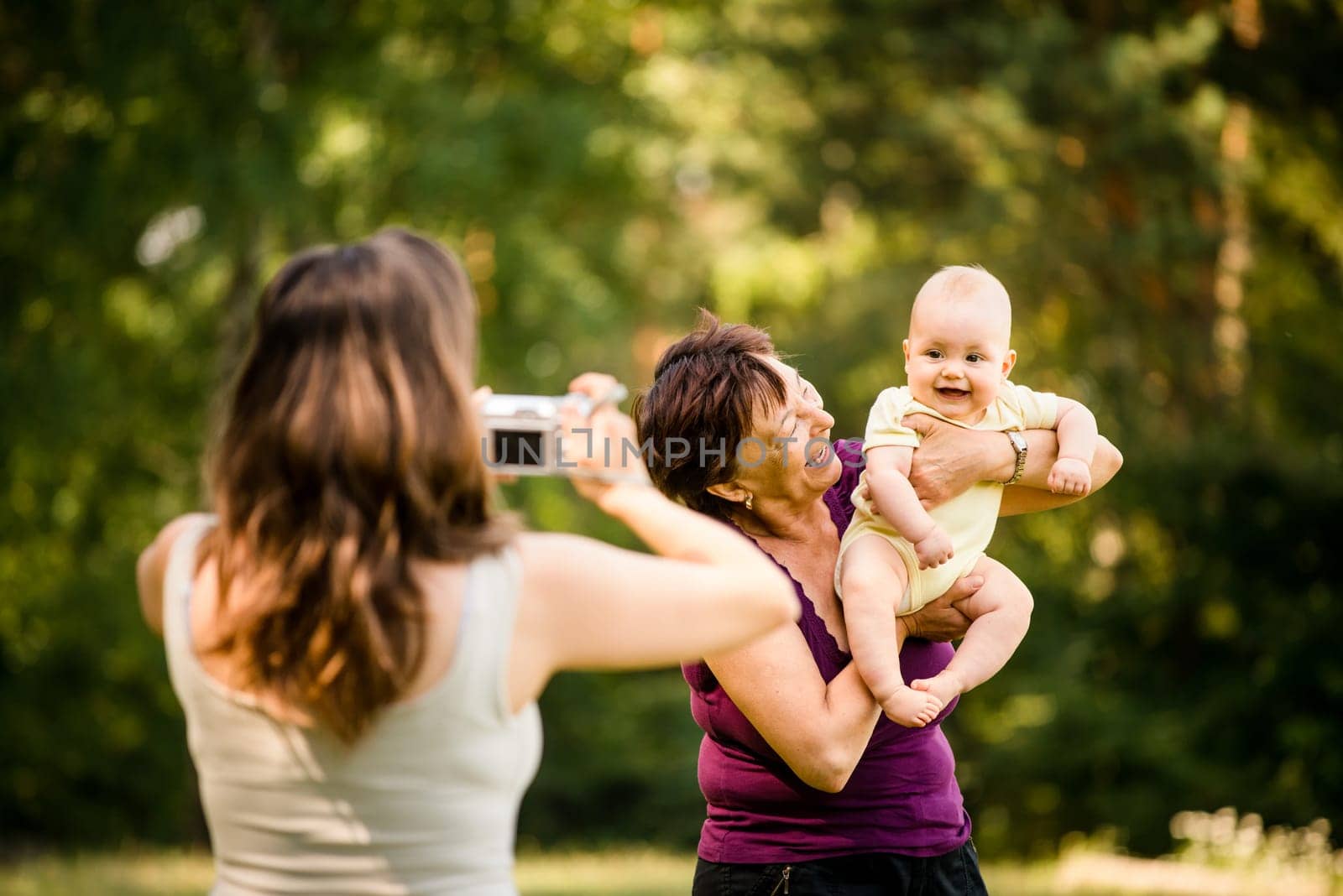 Mother taking photo of grandmother holding her granddaughter - outdoor in nature