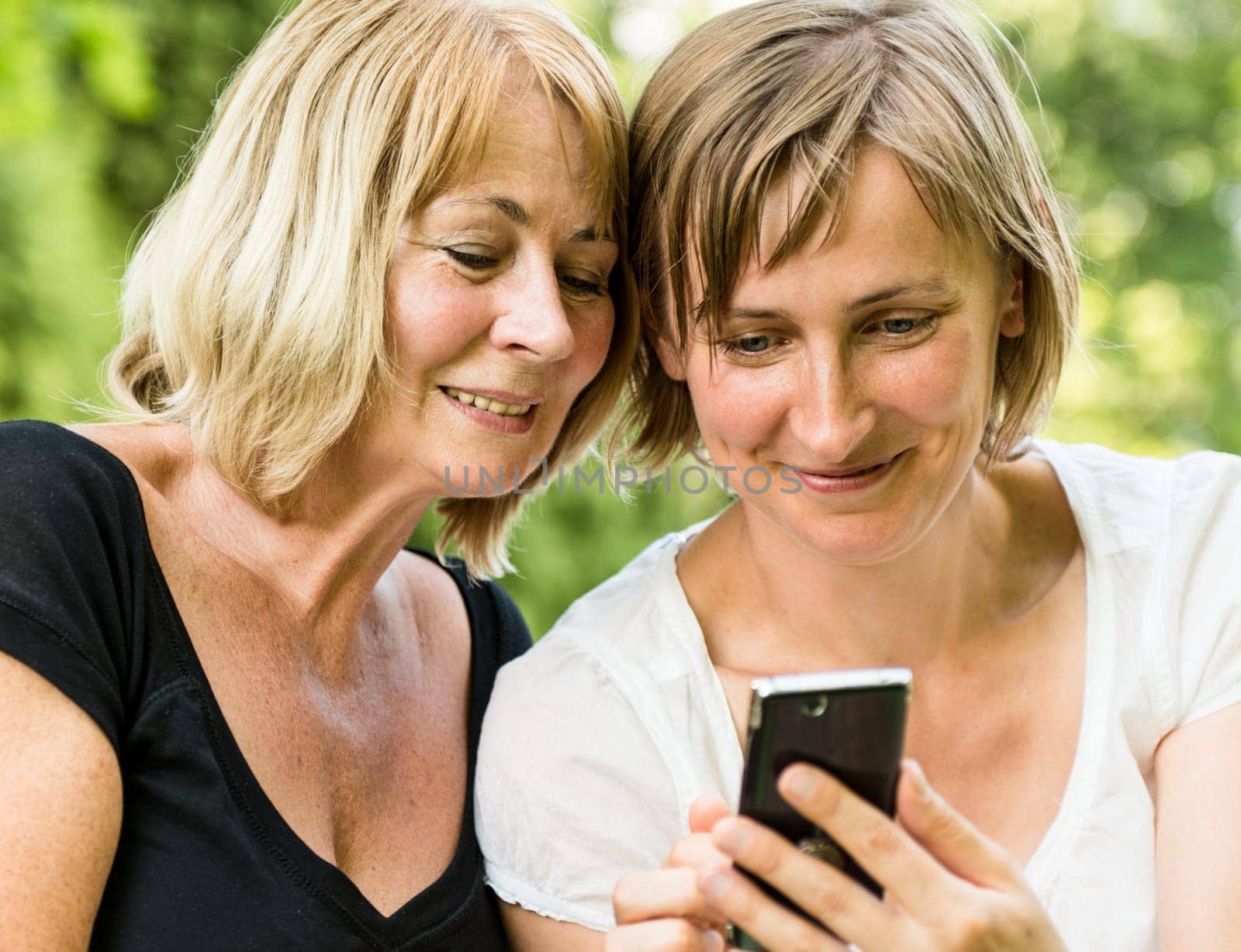 Adult daughter showing on smartphone to her mature mother outdoor in nature