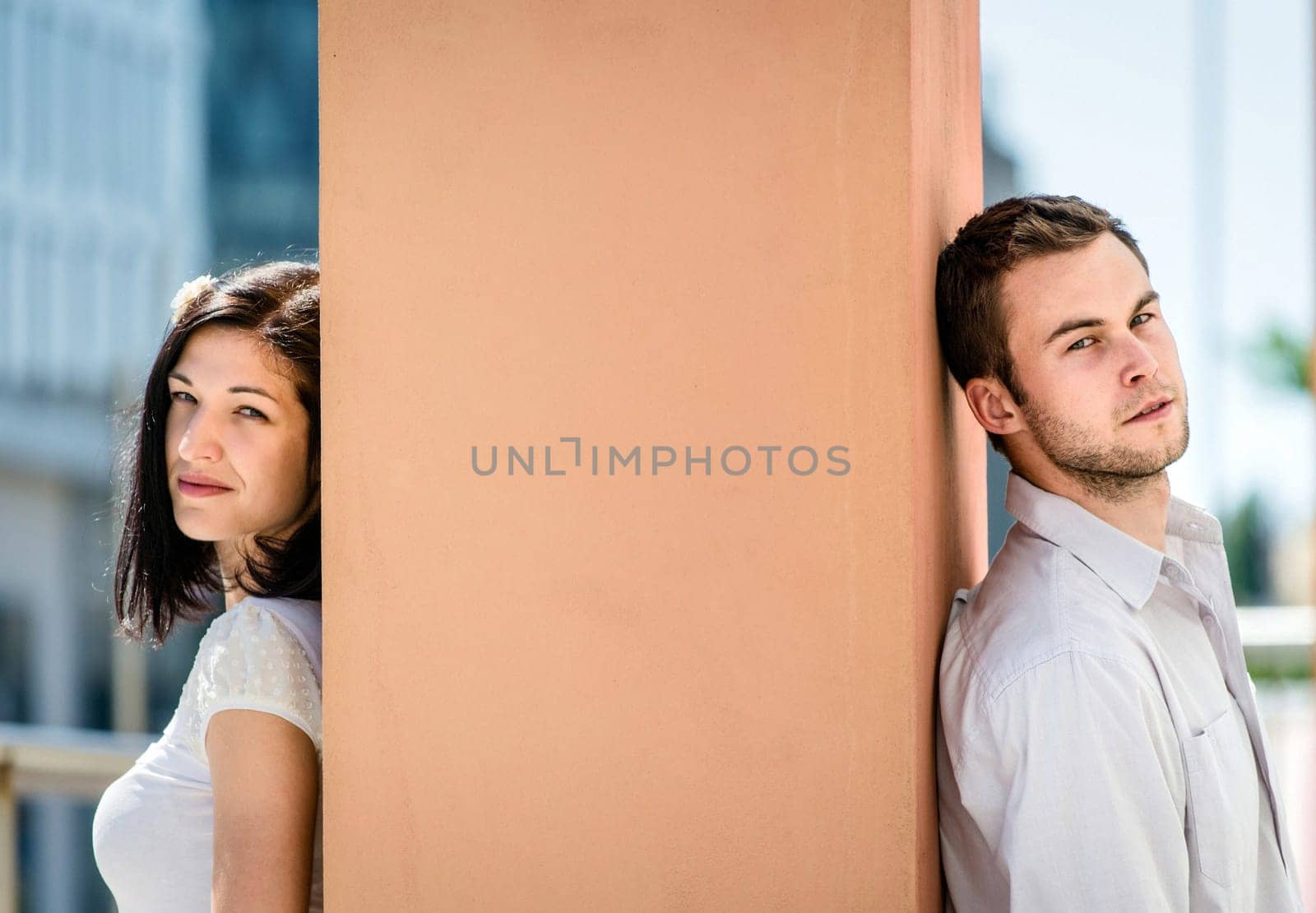 Two people sitting on opposite side of big collumn - outdoor in street