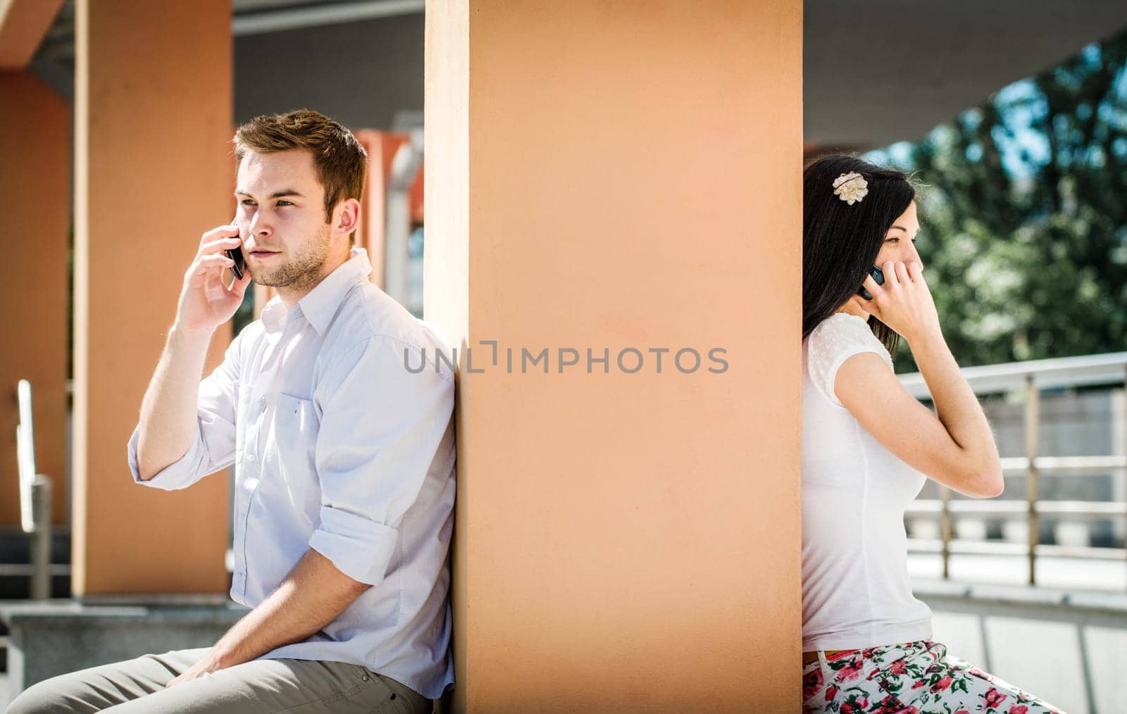 Couple having problems - two people sitting on opposite side of big collumn calling phone