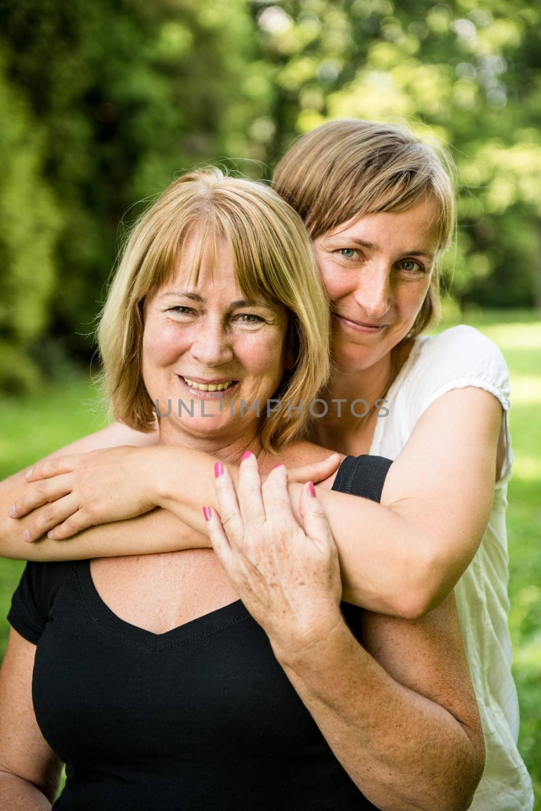 Outdoor portrait of smiling happy senior mother with her adult daughter