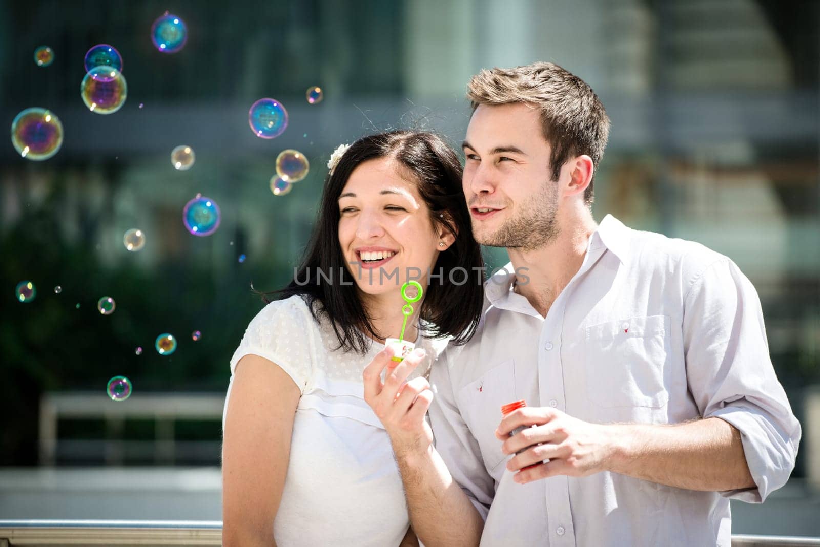 Young couple play together with bubble blower - outdoor in street