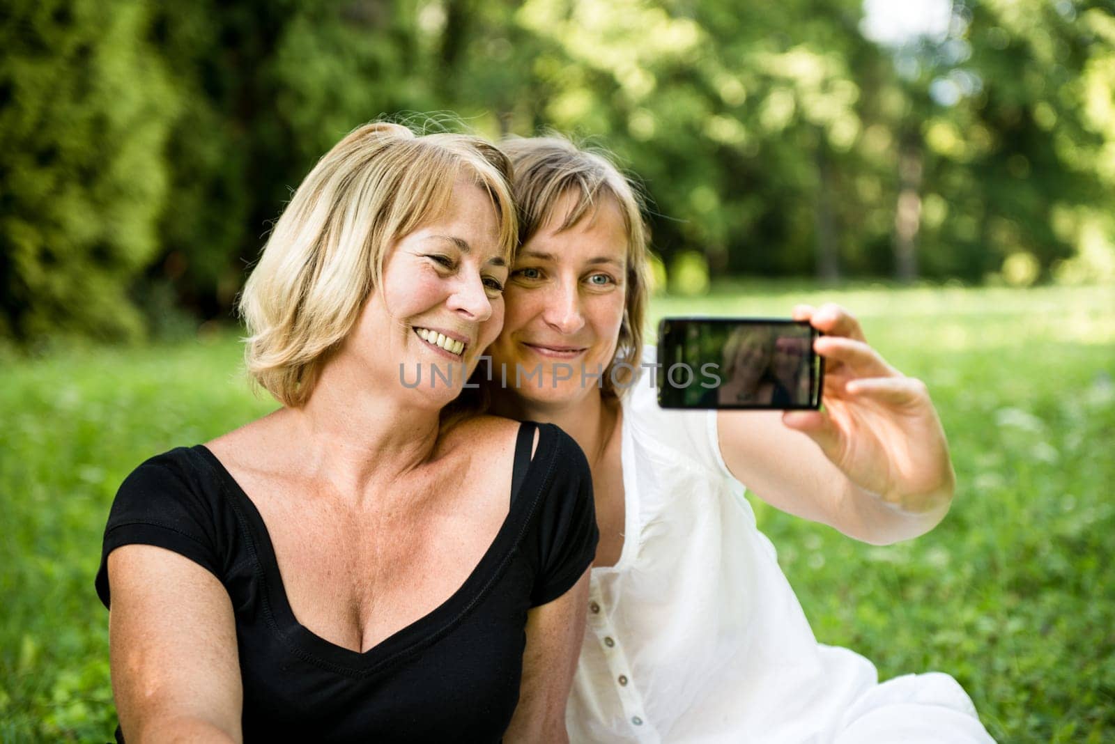 Adult daughter and her senior mother are taking picture with mobile phone