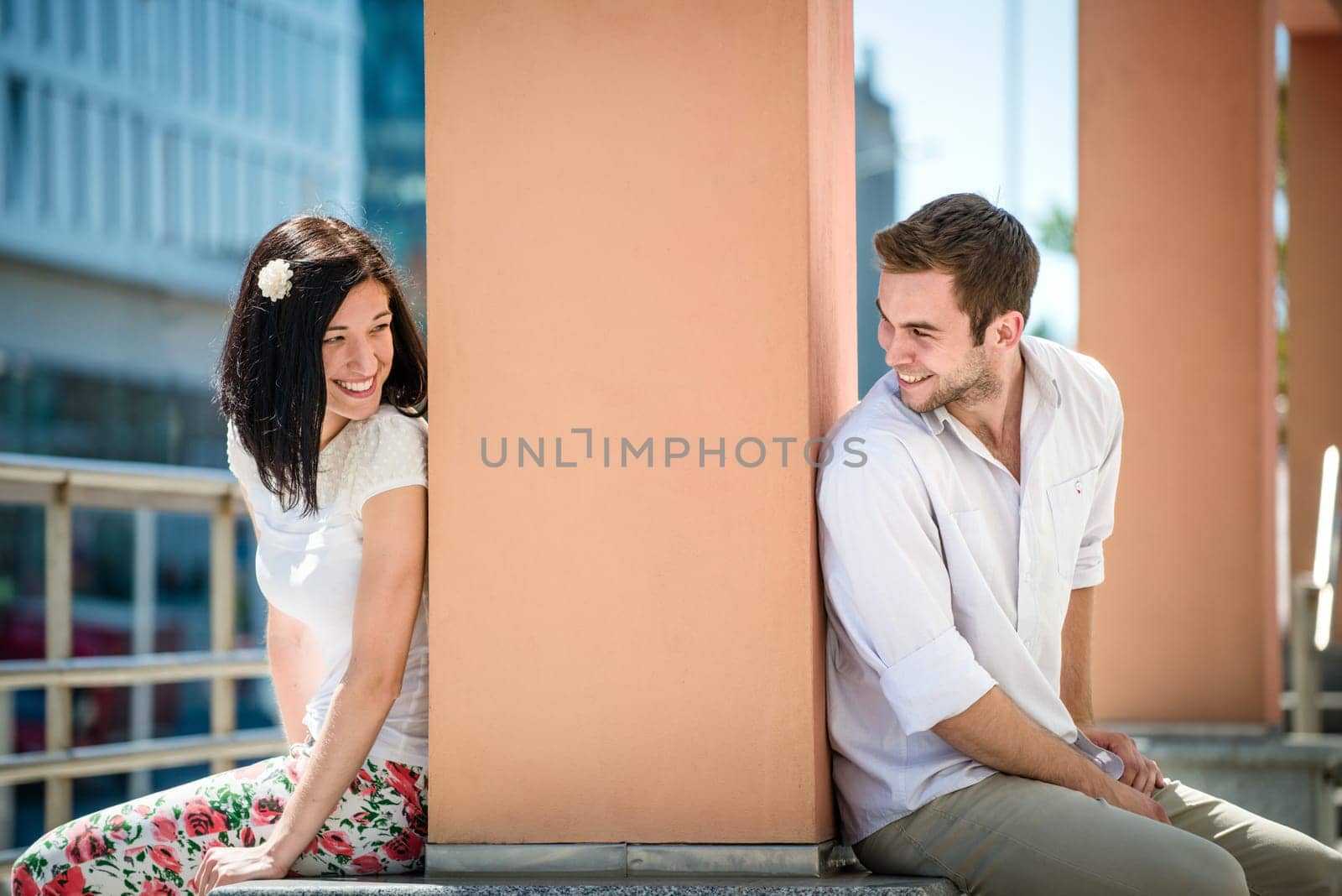 Two people sitting on opposite side of big collumn - outdoor in street