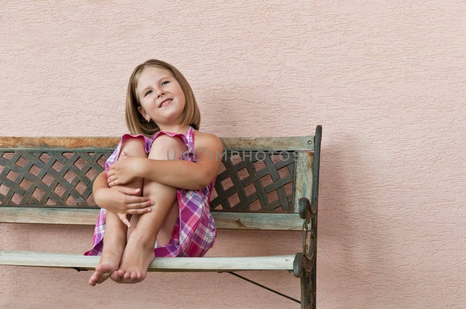 Portrait of cute smiling child sitting on bench and holding her legs