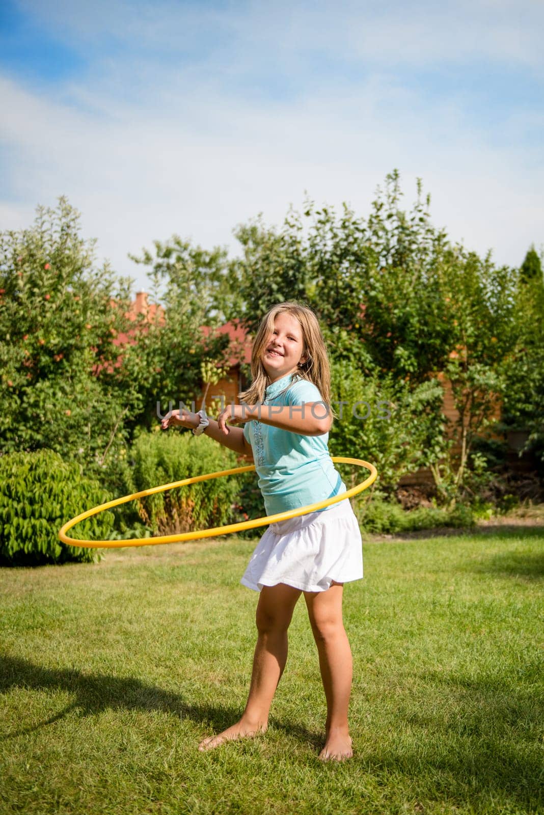 Active child - girl dancing with hoop outdoor in sunny backyard