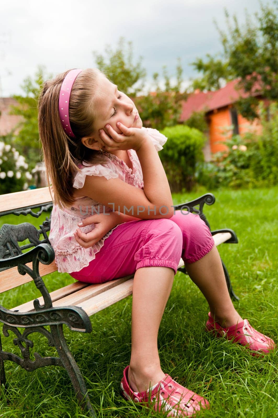 Girl dreaming -  child sitting on bench in garden