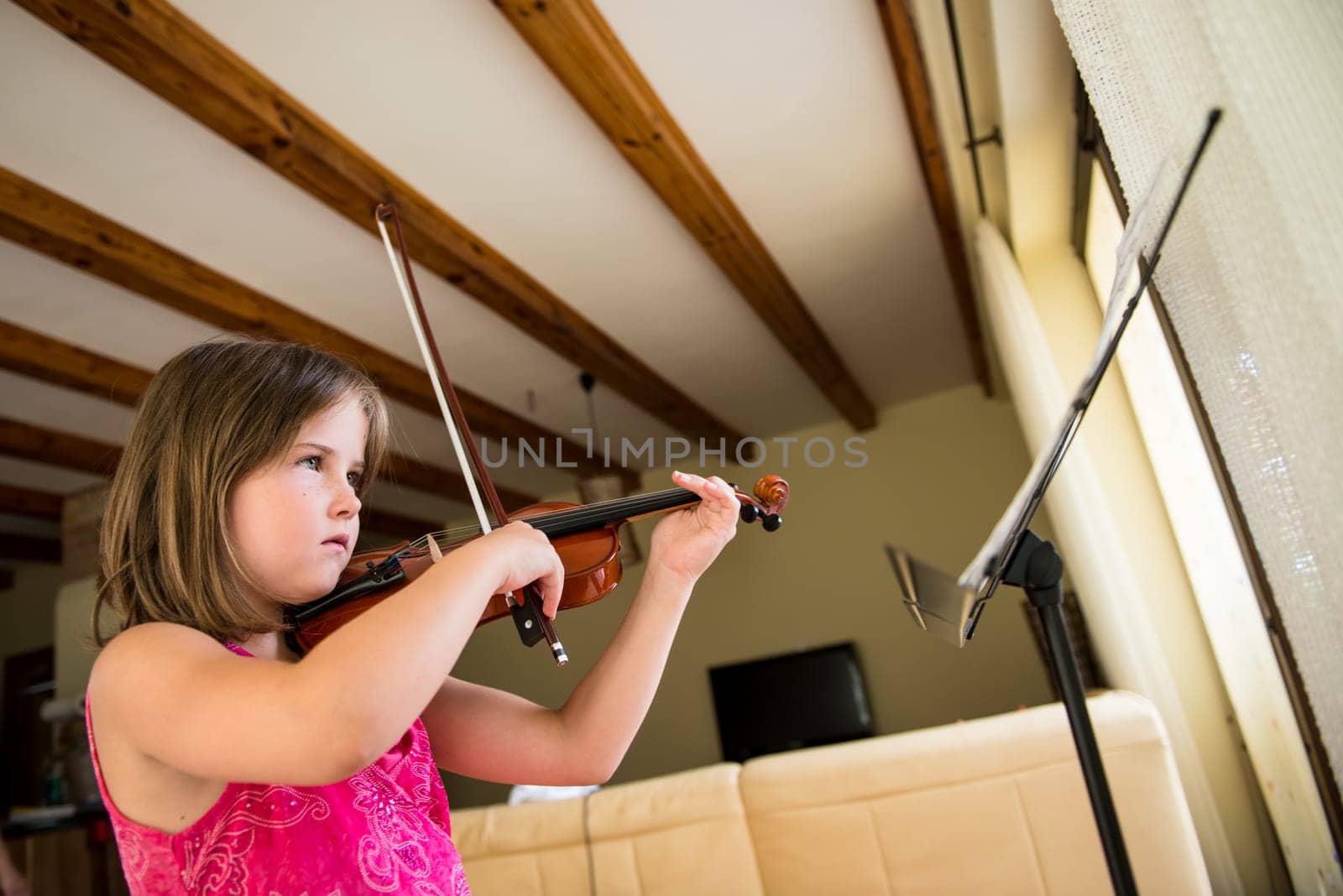 Child (little girl) playing violin indoors at home