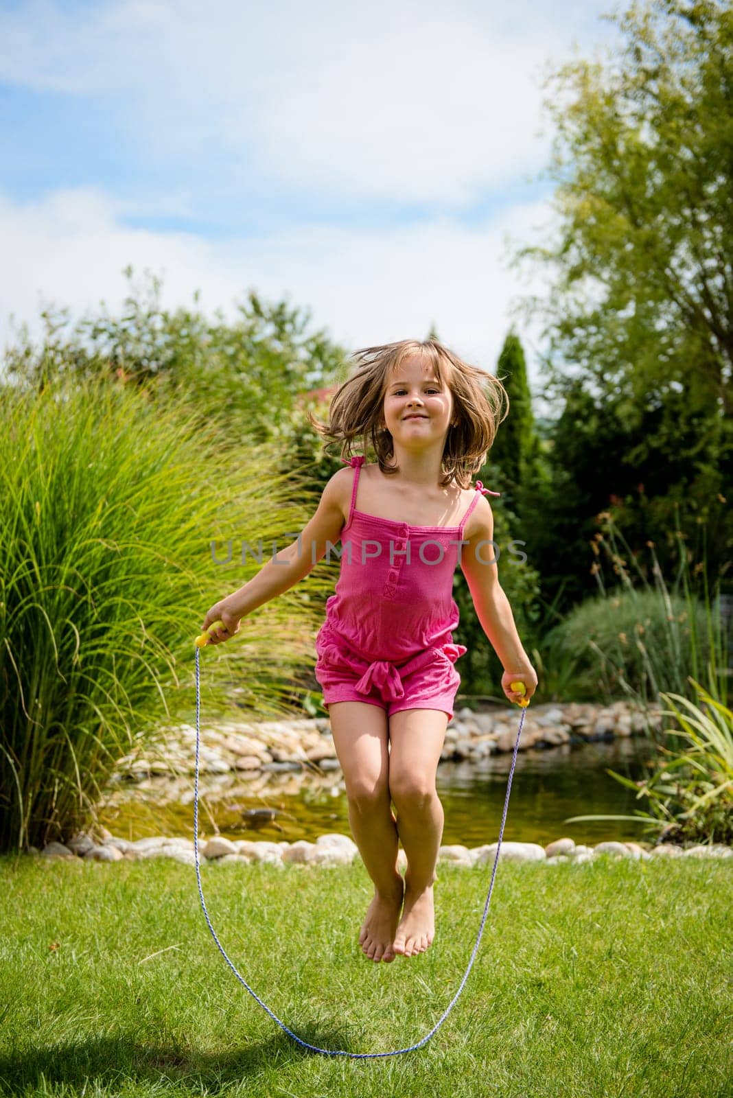 Active child - happy girl jumping with skipping rope outdoor in backyard