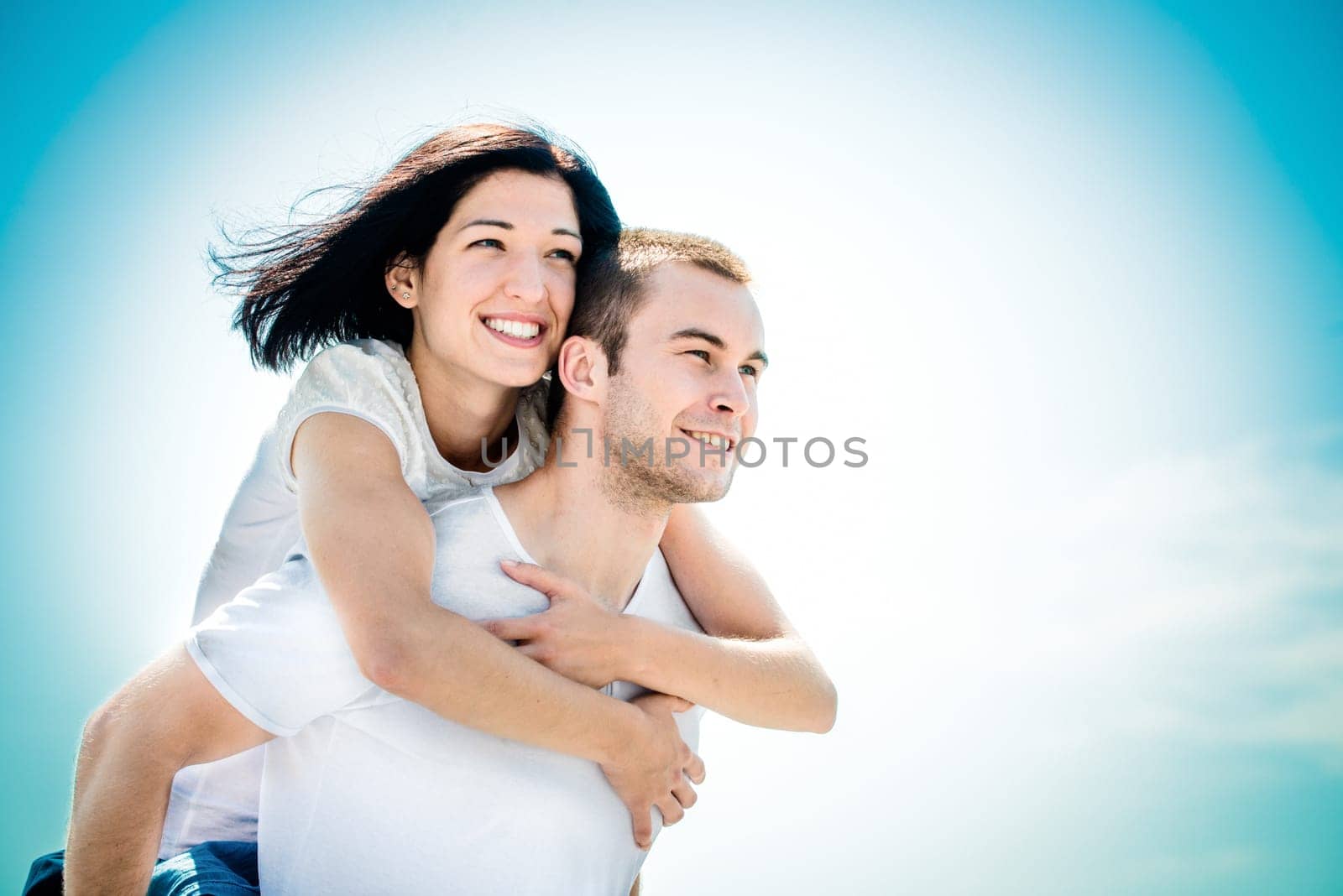 Young couple looking to bright future - happy woman embracing her love around neck