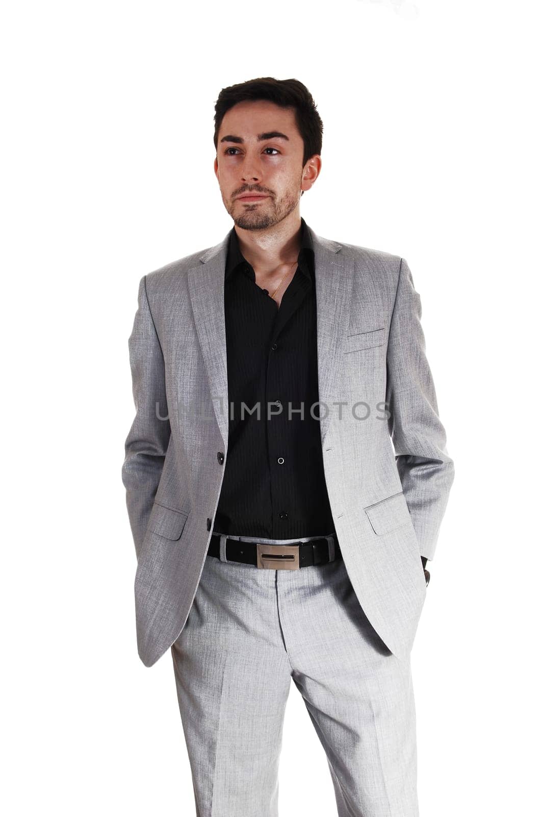 A tall handsome businessman standing for white background in a gray .suit with his hands in his pocket..