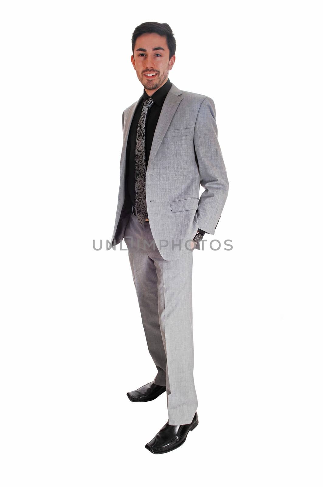 A tall handsome businessman standing for white background in a gray .suit with his hands in his pocket..