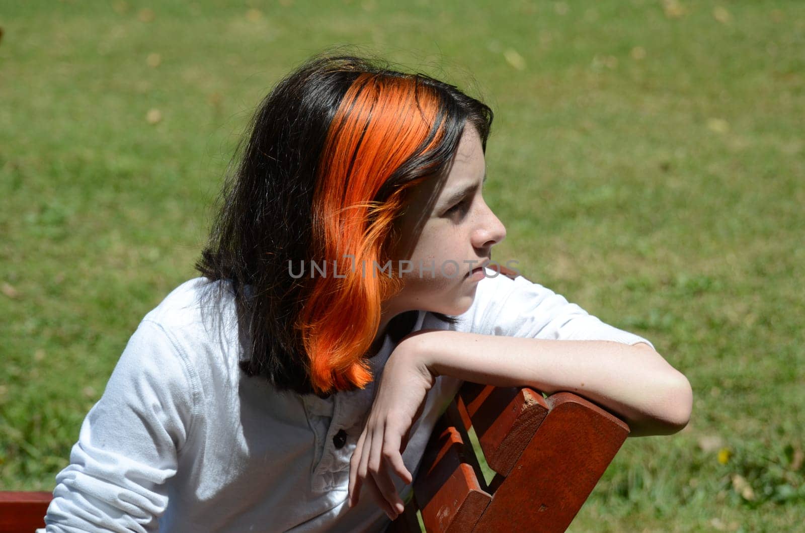 Boy sitting on bench looking right, grass background