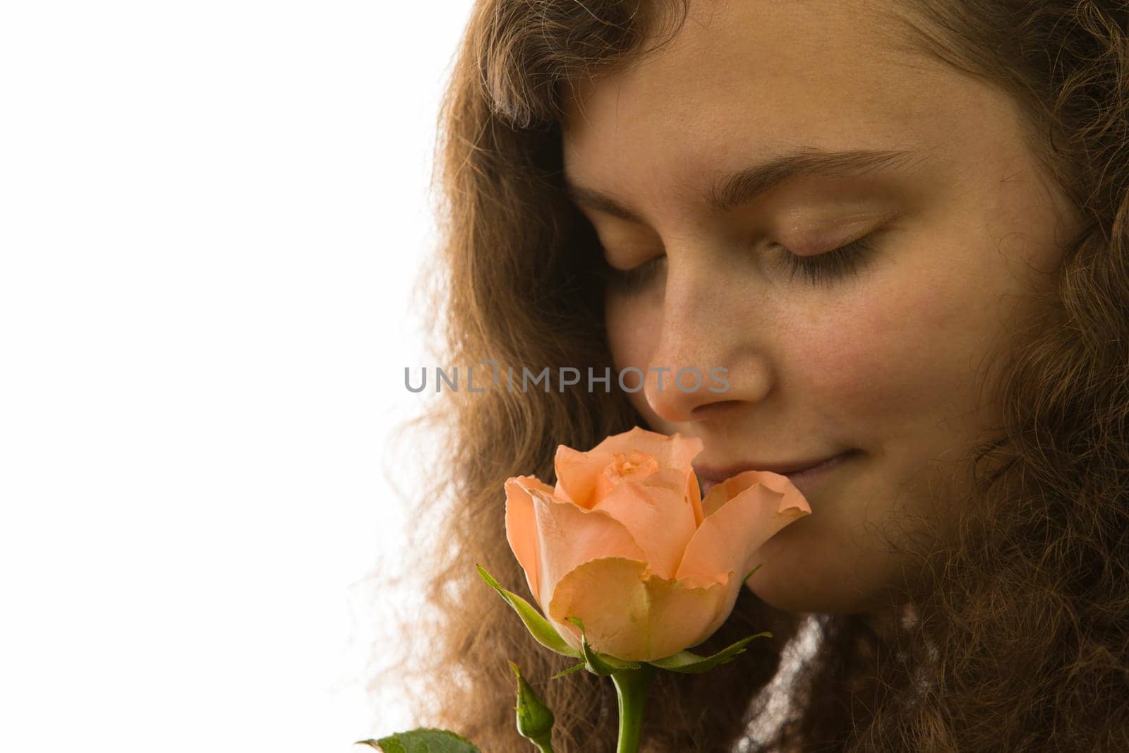 A young pretty woman holds a rose in her hand and smells it