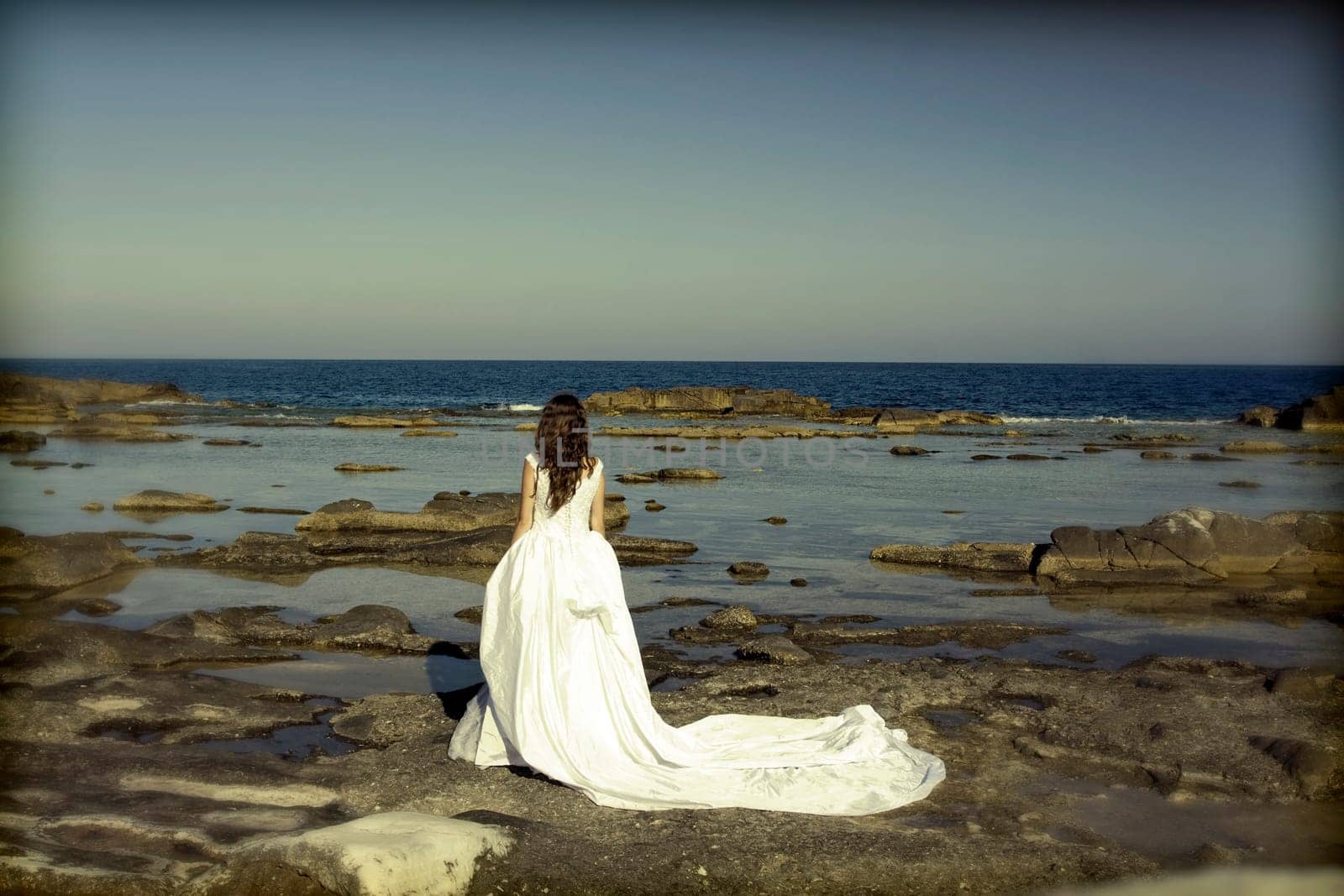 Vintage photo of beautiful bride standing on a cliff on the sea