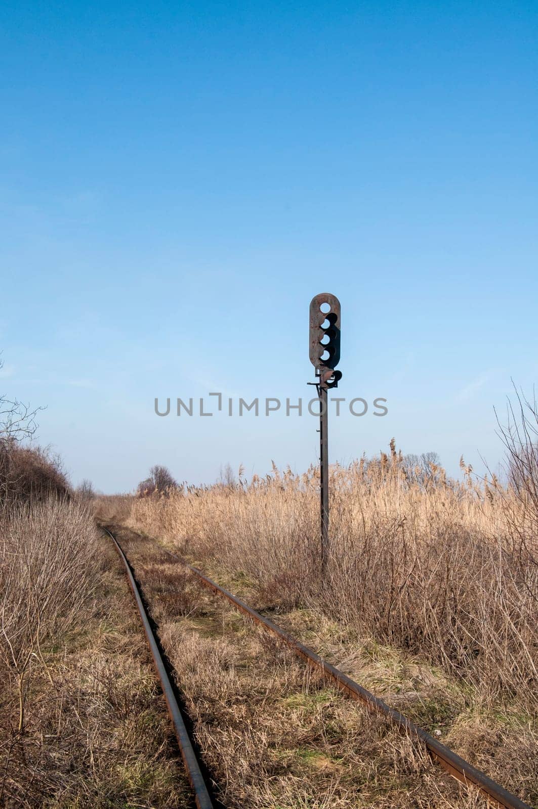 Abandoned rail line and empty railway traffic light in dry grass field