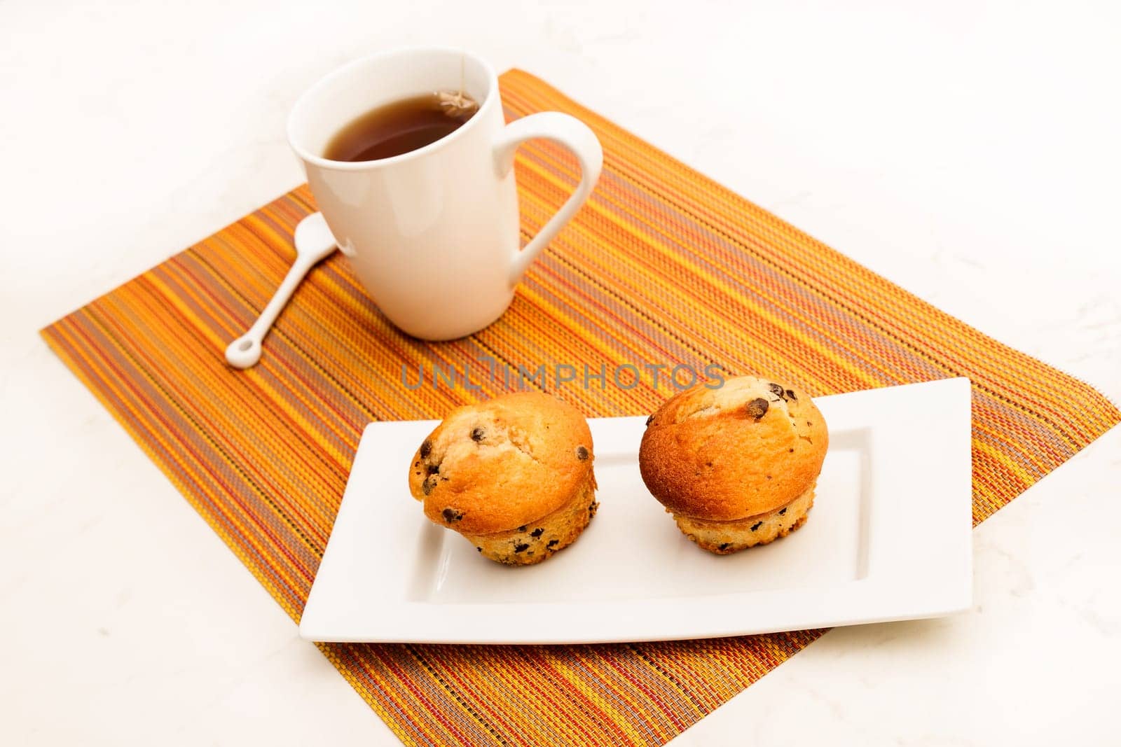 Vanilla with chocolate chips Muffins on a white plate with  a cup of tea.