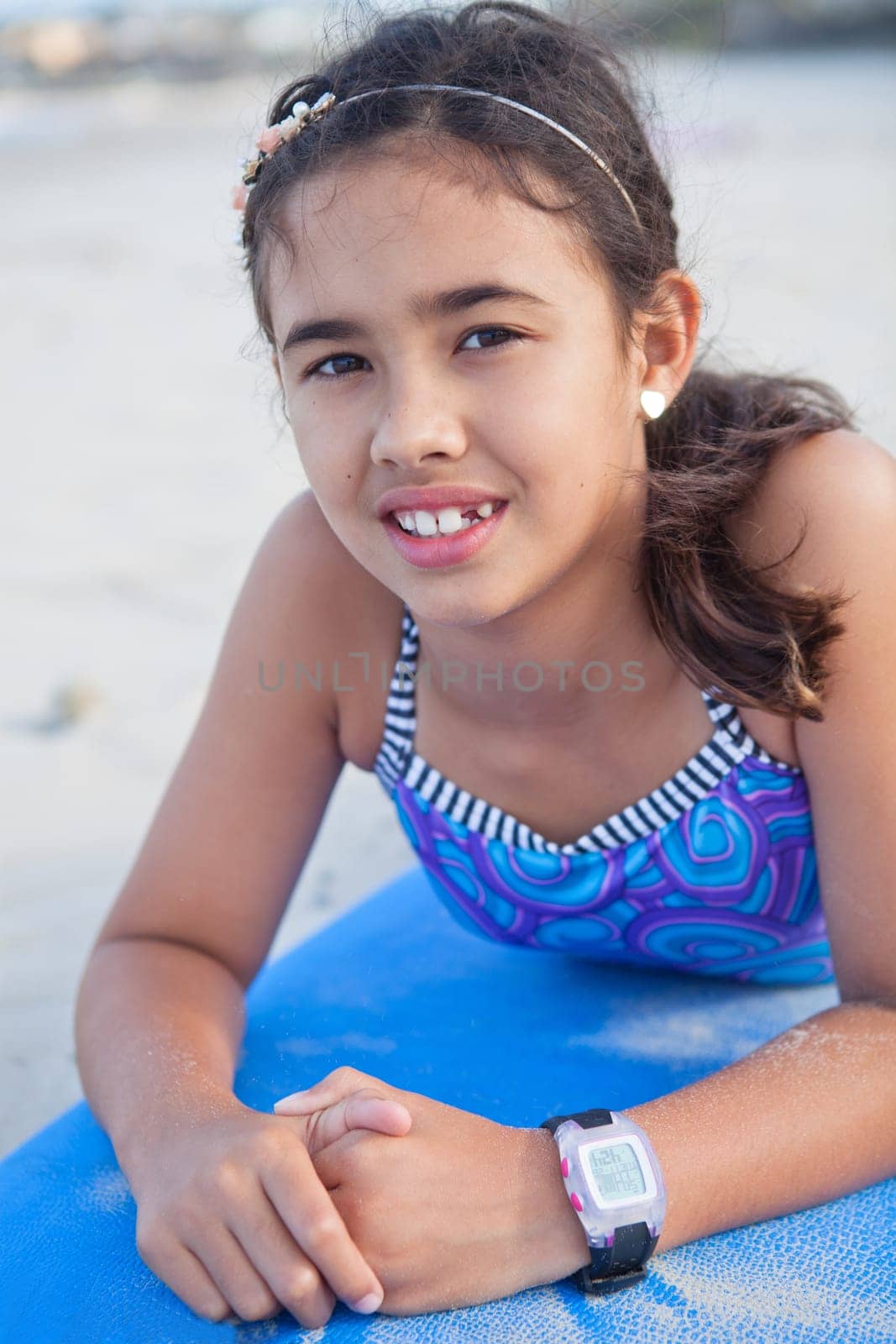 Closeup portrait of cute young girl lying on blue surfboard on the beach