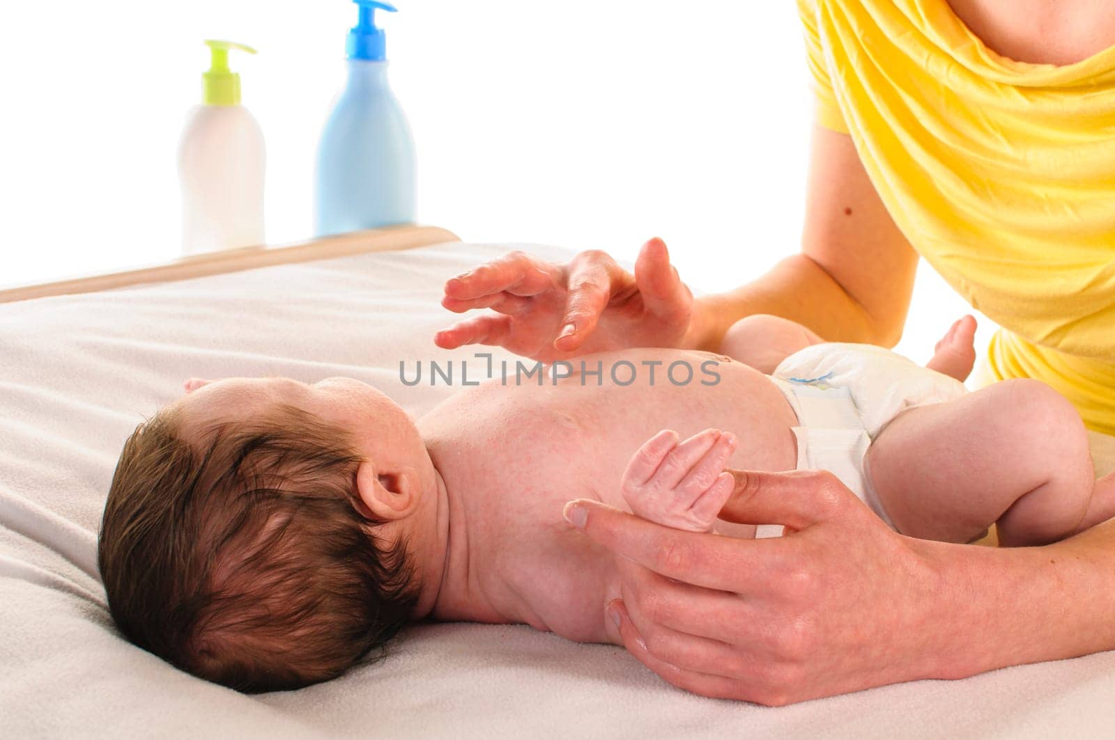 Mother with her newborn baby does infant care at the changing table,exposed against a white background.