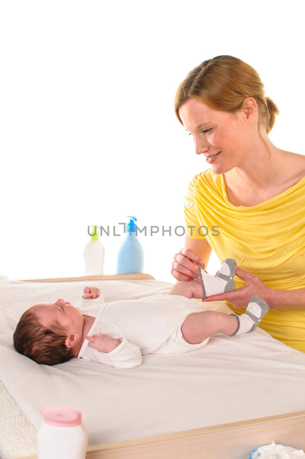 Mother with her newborn baby does infant care at the changing table,she puts socks on the baby,exposed against a white background.