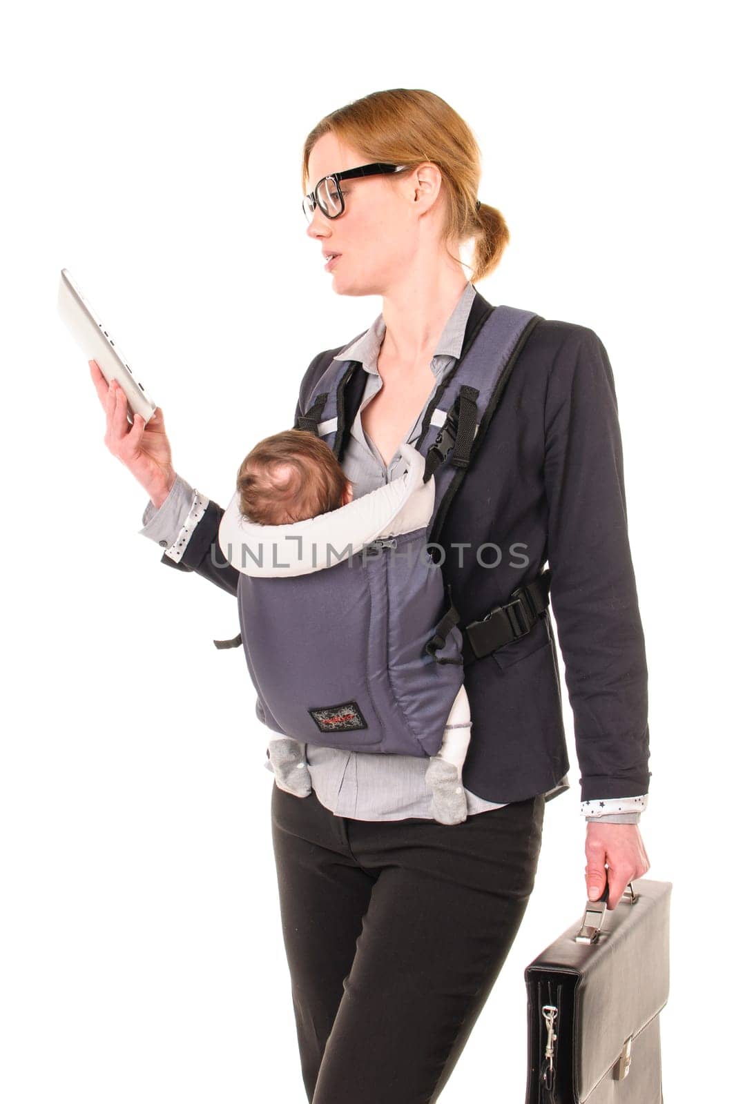 Adult businesswoman woman wears shirt and jacket and has an infant in a baby carrier while reading an email on her tablet PC,cropped against a white background.