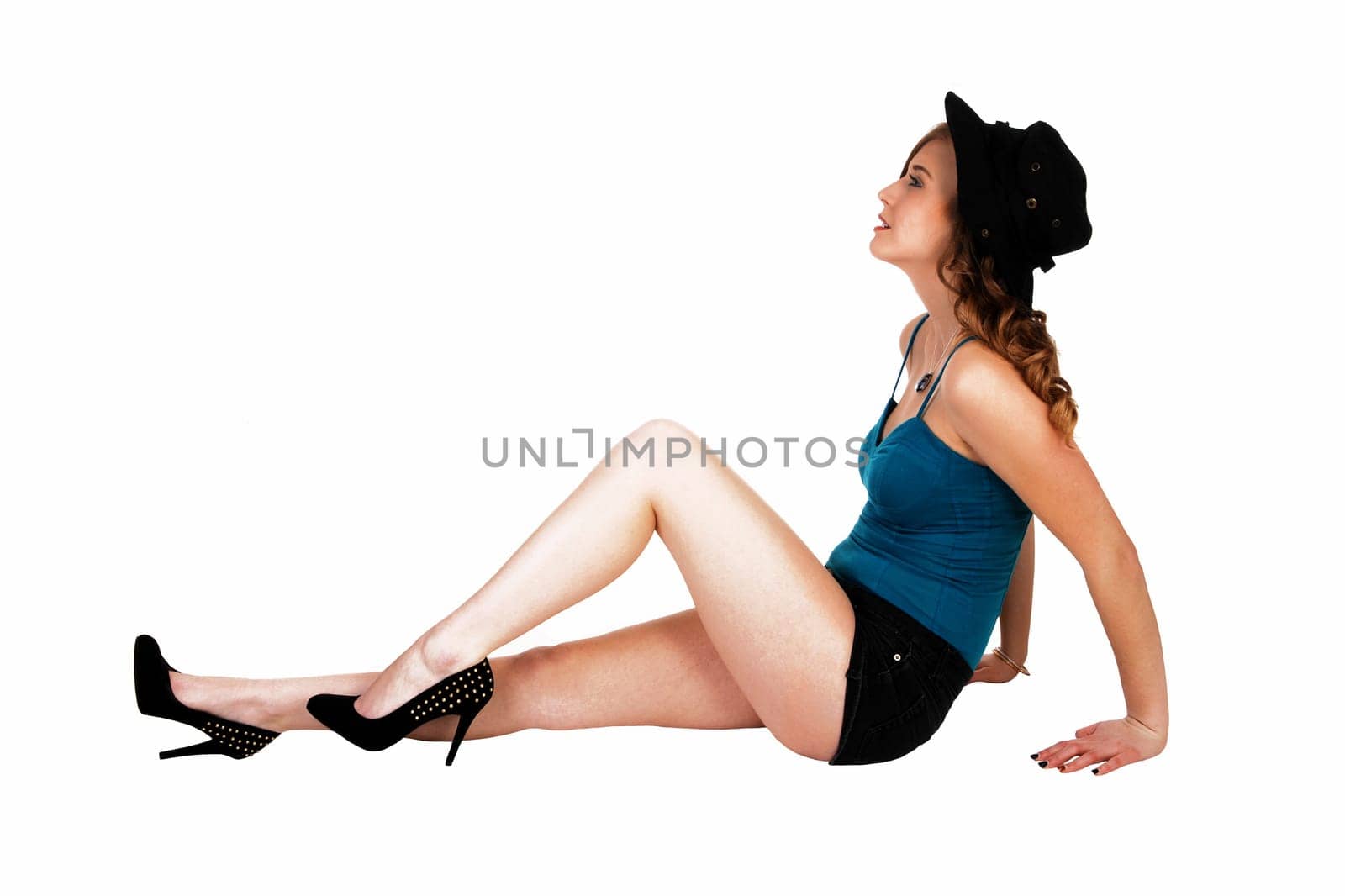 A young pretty woman sitting on the floor for white background with a black.hat and high heels..