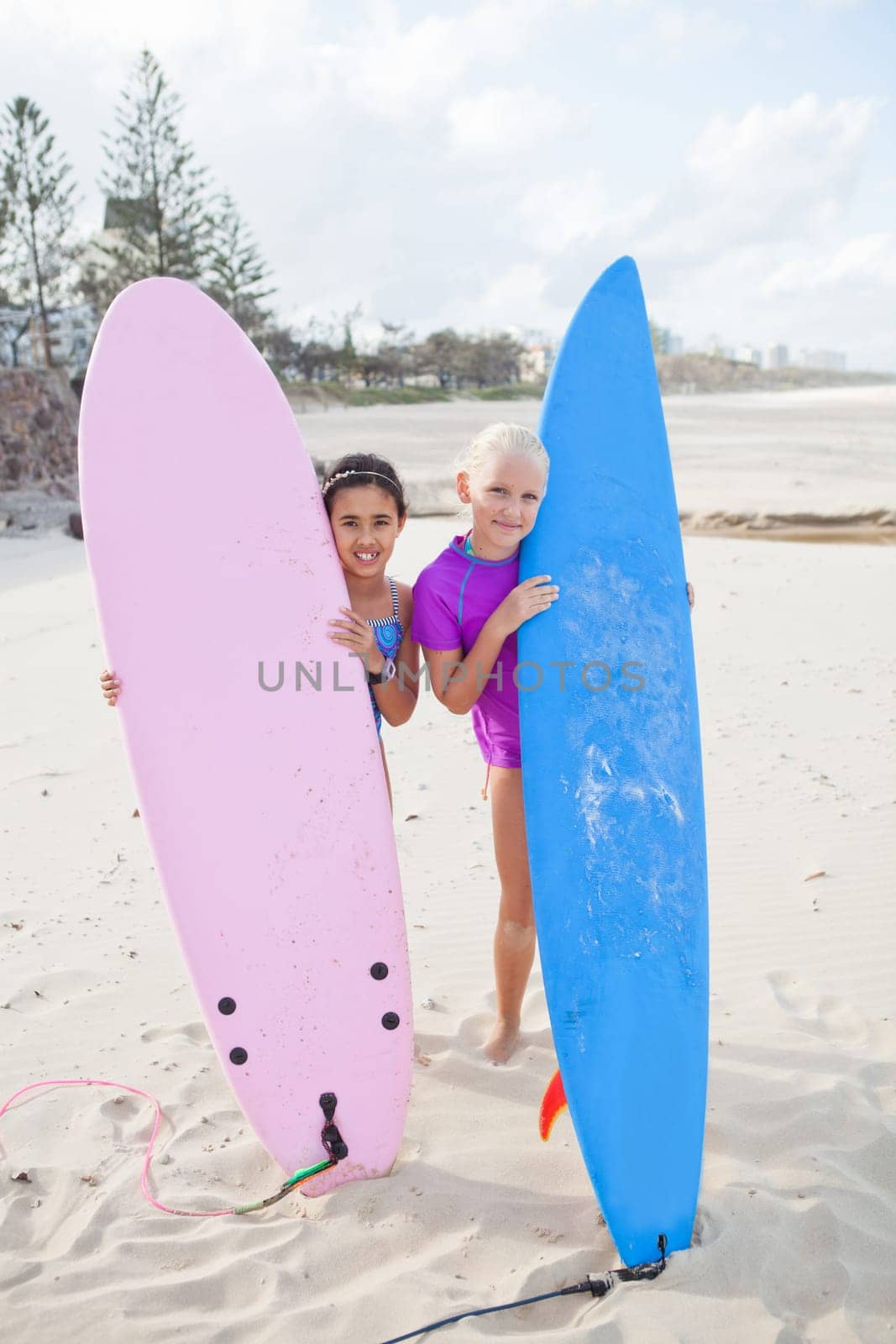 Two cute smiling young girls holding surfboards upright at the beach