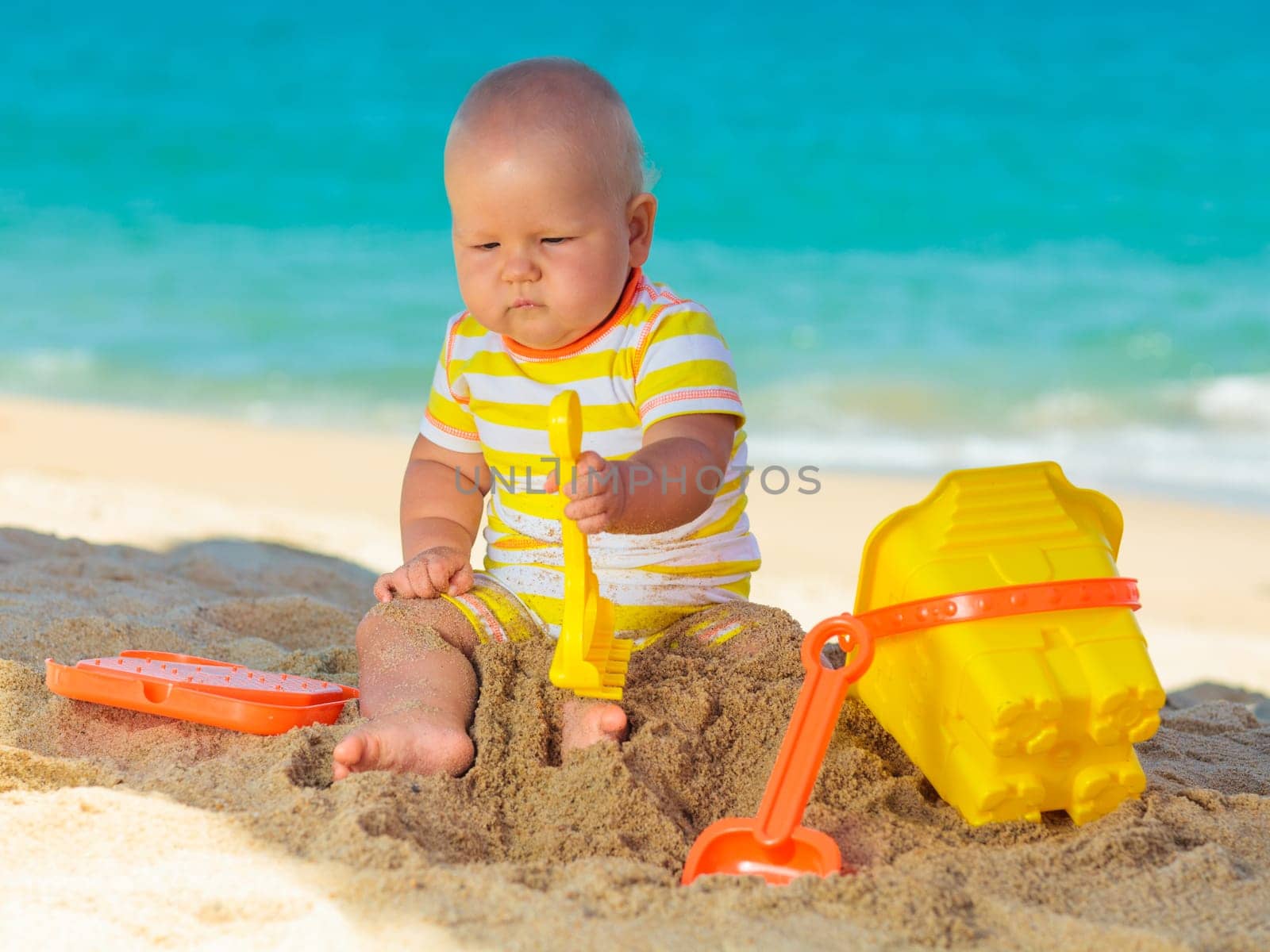 Cute baby on the tropical beach playing toys
