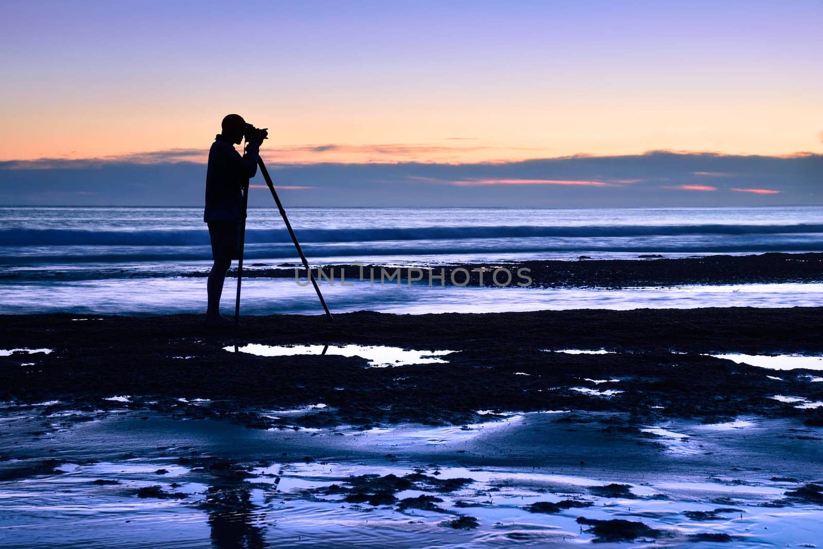 The silhouette of a man photographed with a tripod at dusk by the sea