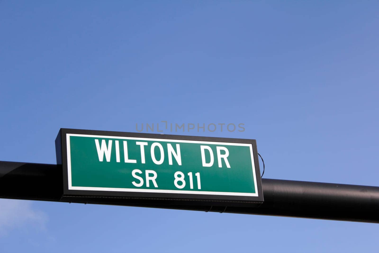 Green and white street sign over Wilton Drive also called State Route 811, seen in Wilton Manors, Florida on a sunny, blue sky day.