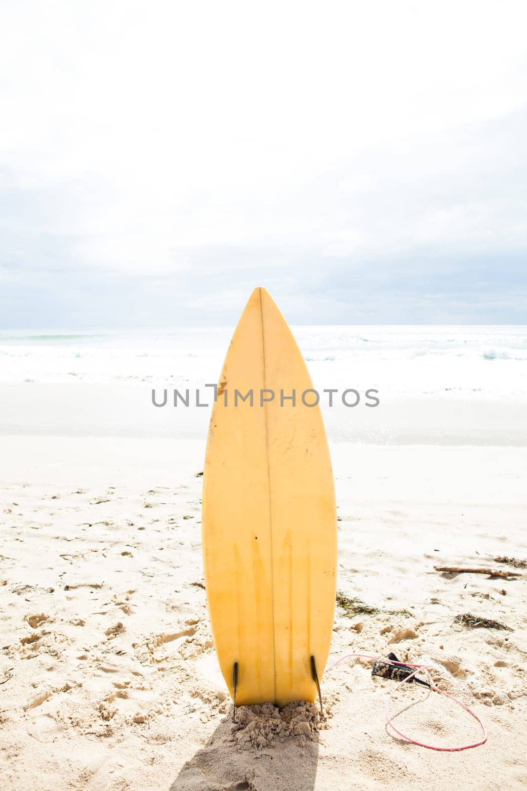 Yellow surfboard standing upright in sand on beach with ocean and sky in background