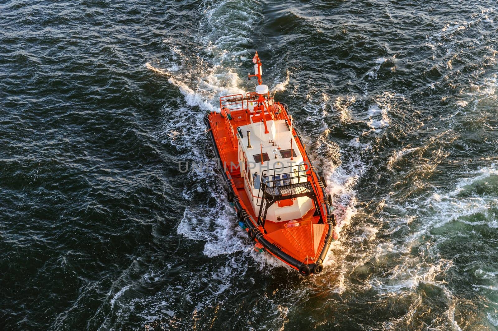 orange and white coast guard lifeboard photographed from bird's eye view,visible sunset sunrays,sea and waves.