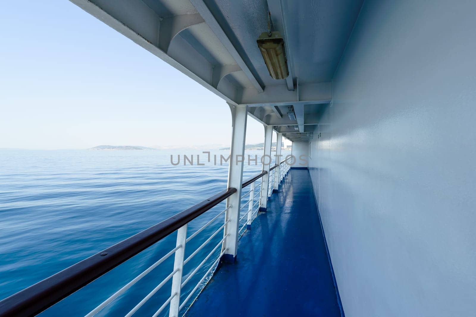 fragment of a ship deck or passenger ferry with visible railing and blue sea,in background cloudless summer sky.