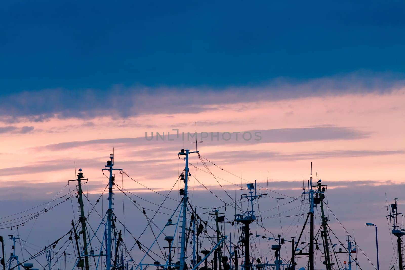 plenty of masts of fishing boats and sailing boats in sunset background,visible ropes,rigging,radars and navigation aerials,space fot text.
