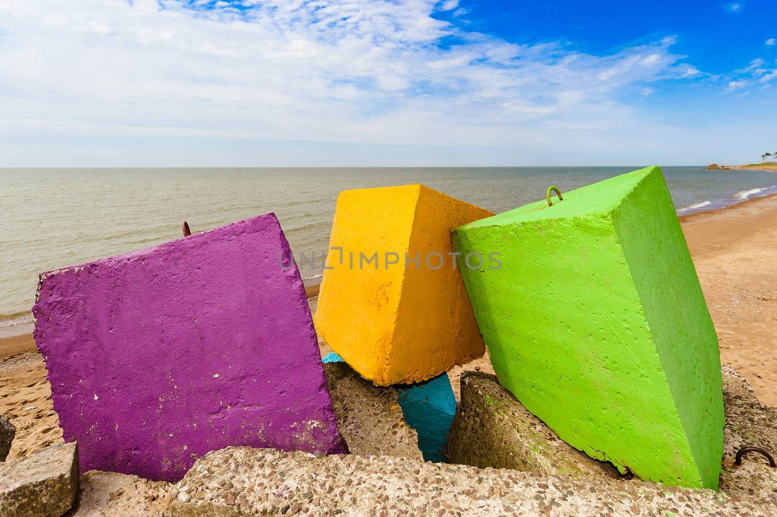 three different colors - purple,yellow and green concrete blocks on a background,cloudless sky,yellow sand and coastline.