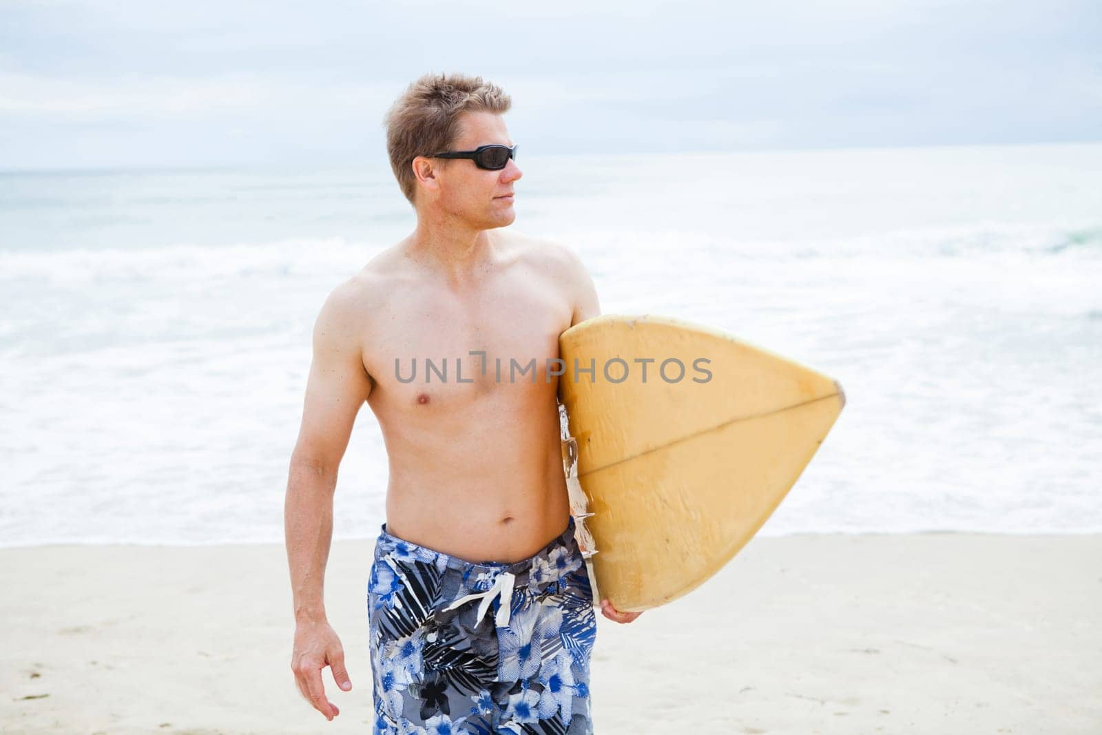 Relaxed and focused looking male surfer walking on beach while carrying surfboard