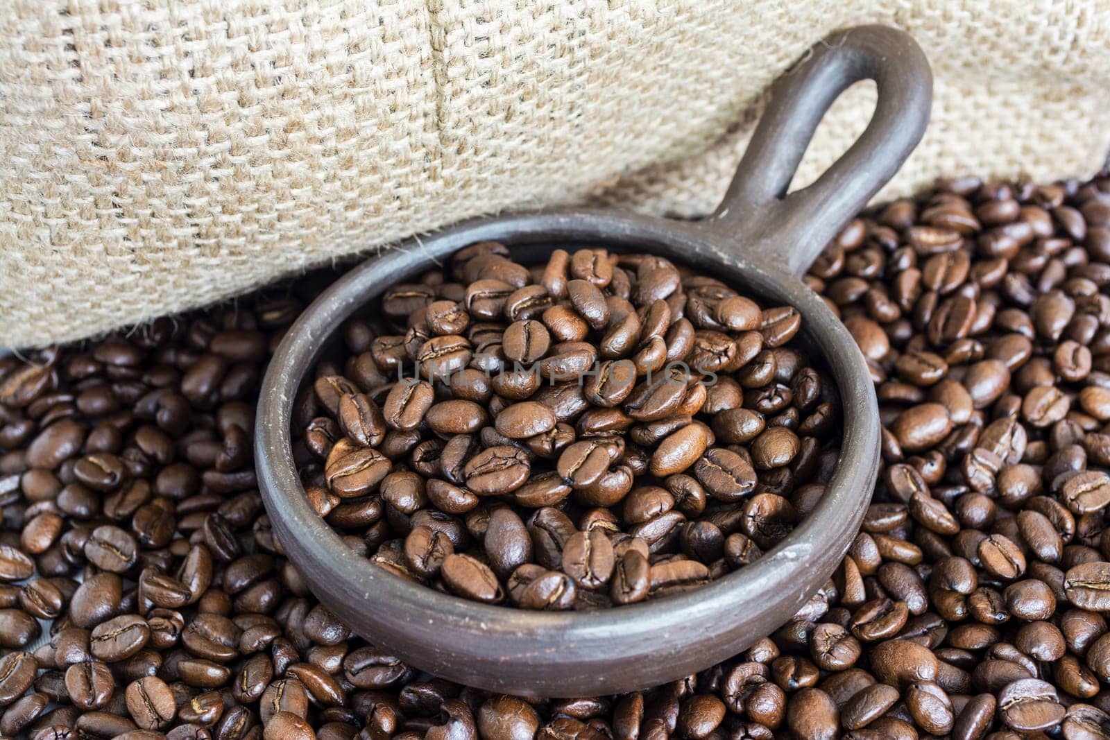 Coffee beans in a small clay pot. Image has a background of jute fibers