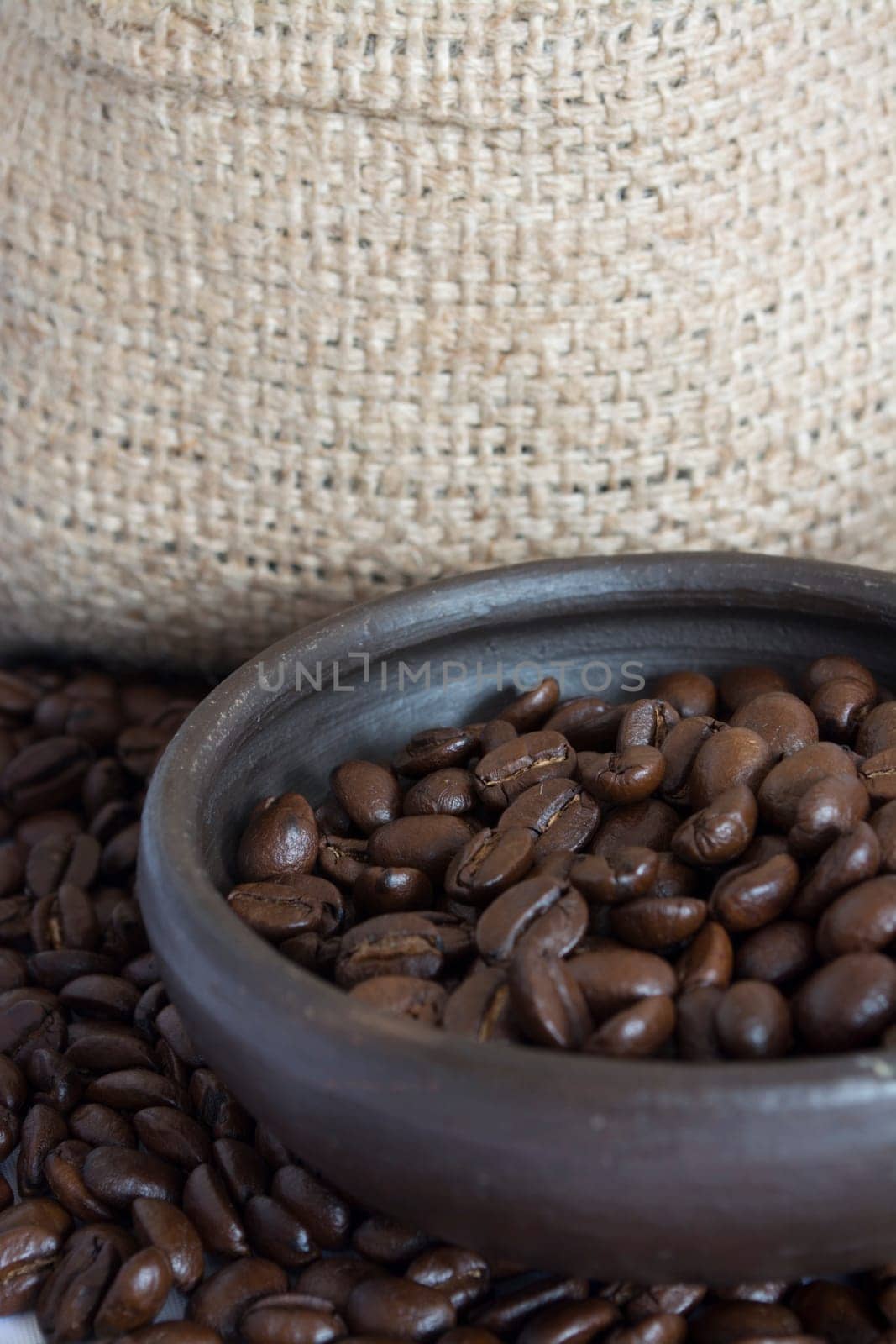 Coffee beans in a small clay pot. Image has a background of jute fibers
