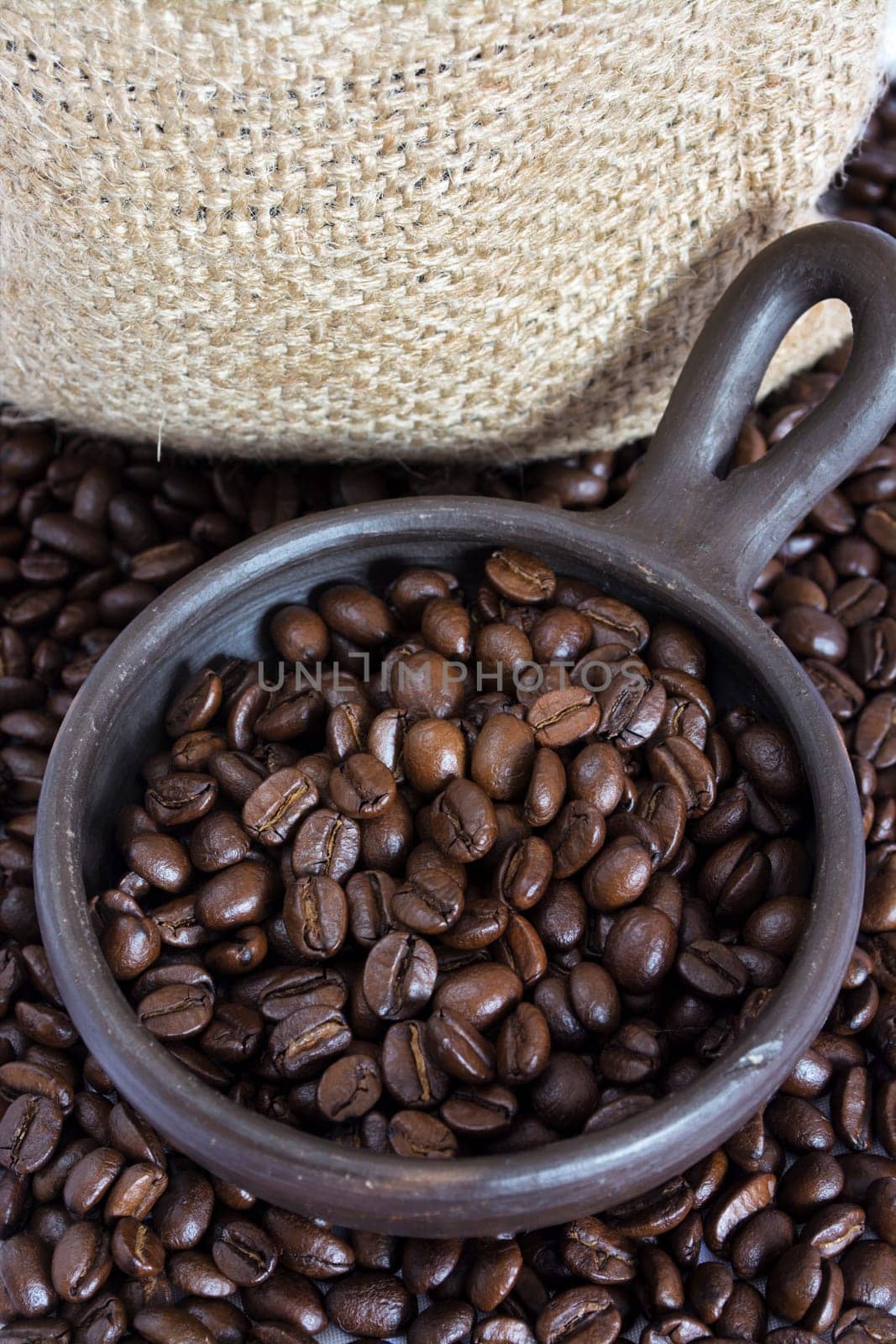 Coffee beans in a small clay pot. Image has a background of jute fibers
