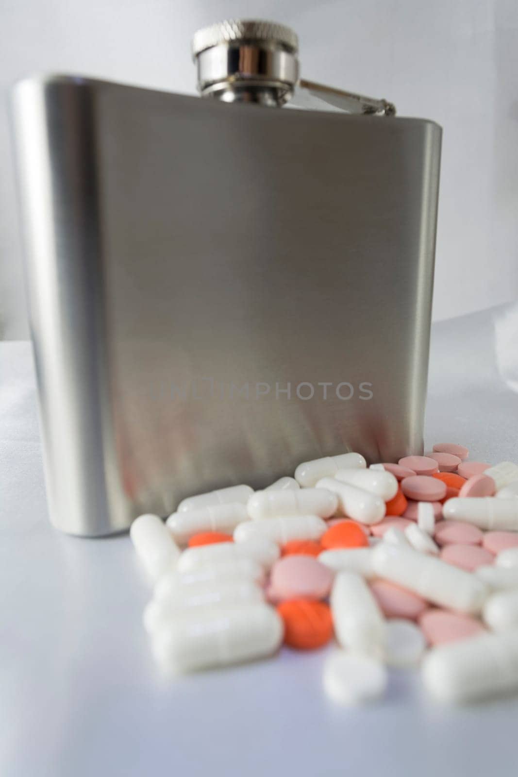 Silver metal flask with pills on a grey background.