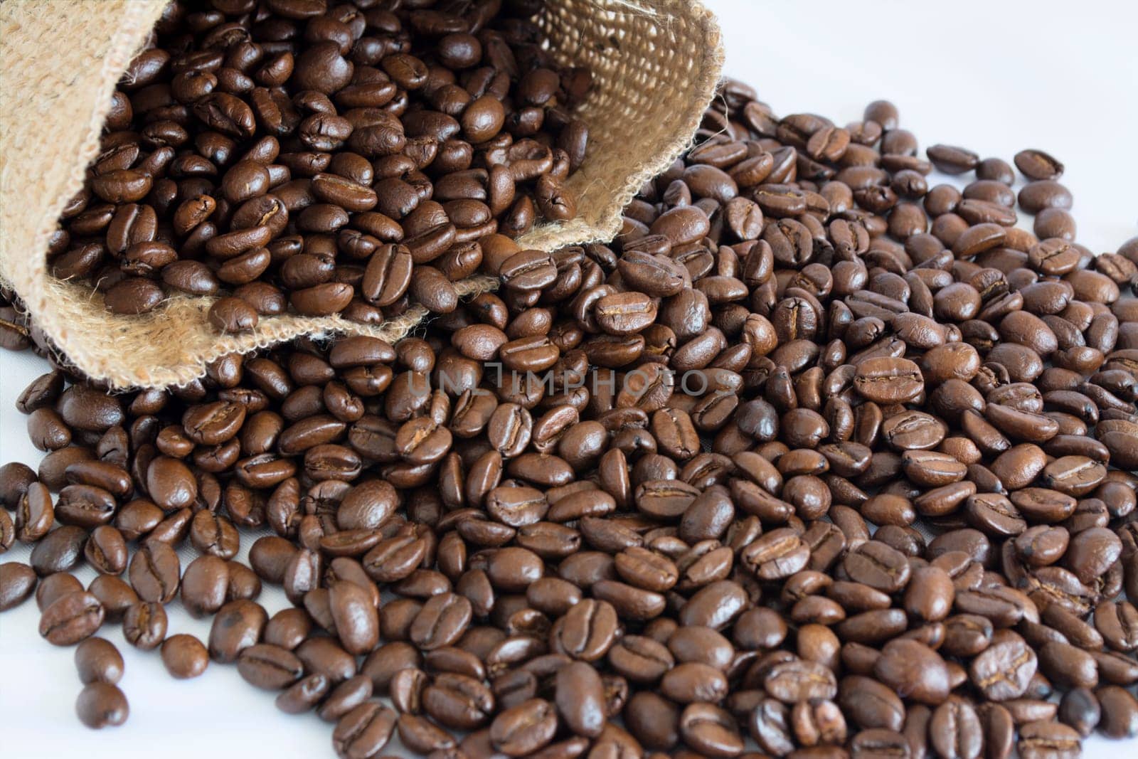 Jute bag and scattered coffee beans on a white background