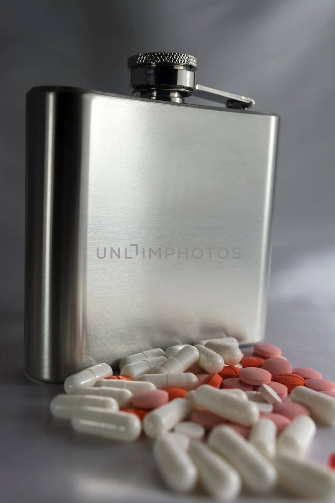 Silver metal flask with pills on a grey background.