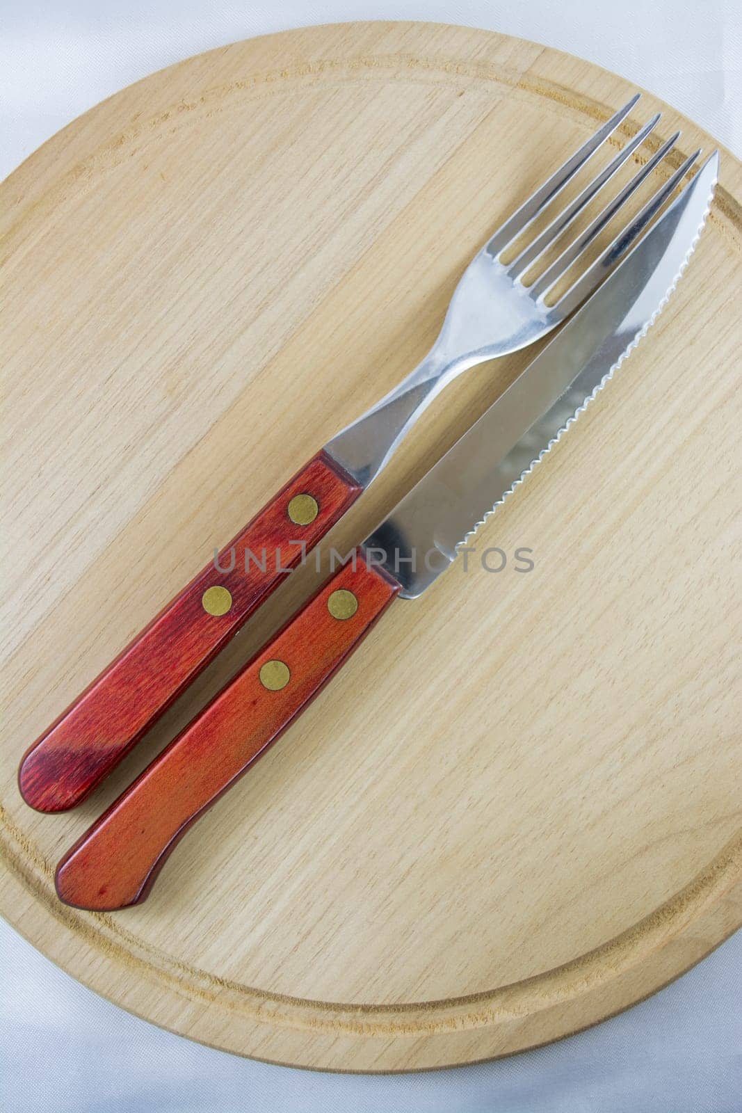 Fork and knife with red wooden handle on a plate of natural wood.