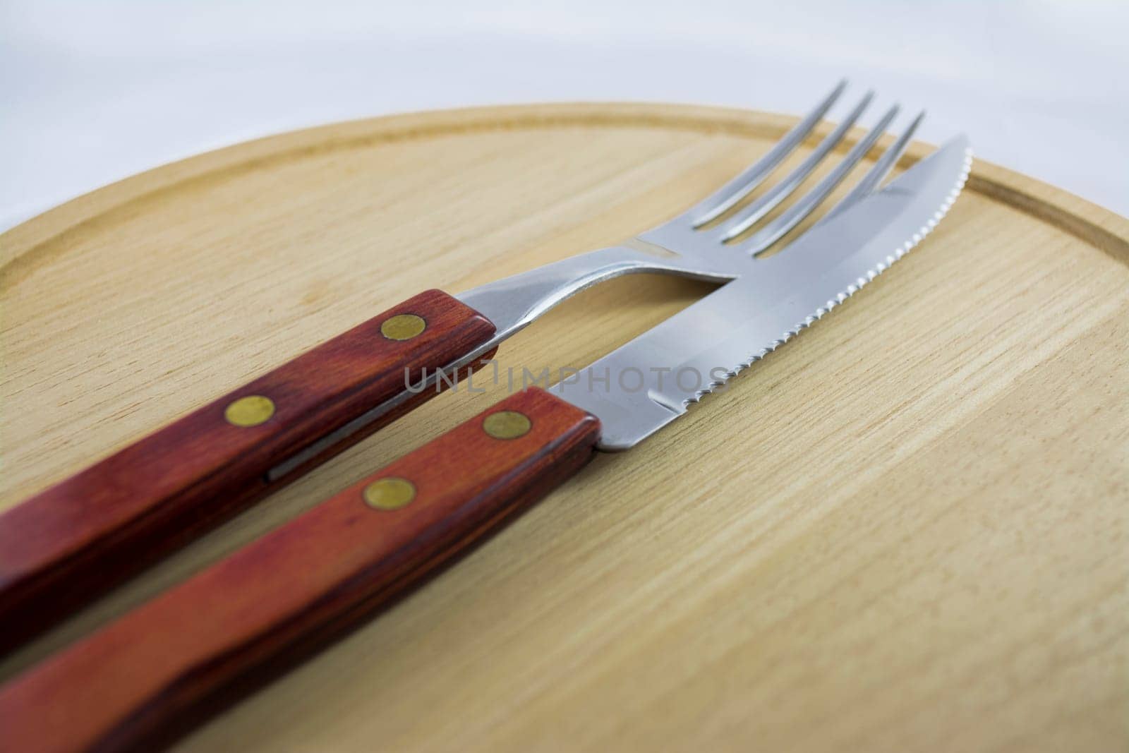 Fork and knife with red wooden handle on a plate of natural wood.