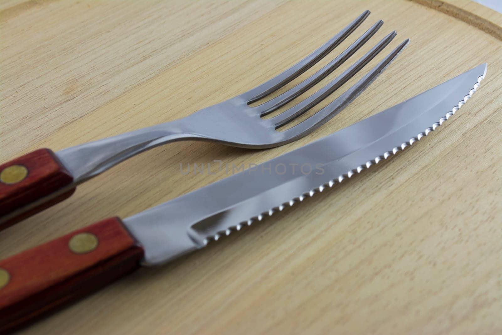 Fork and knife with red wooden handle on a plate of natural wood.