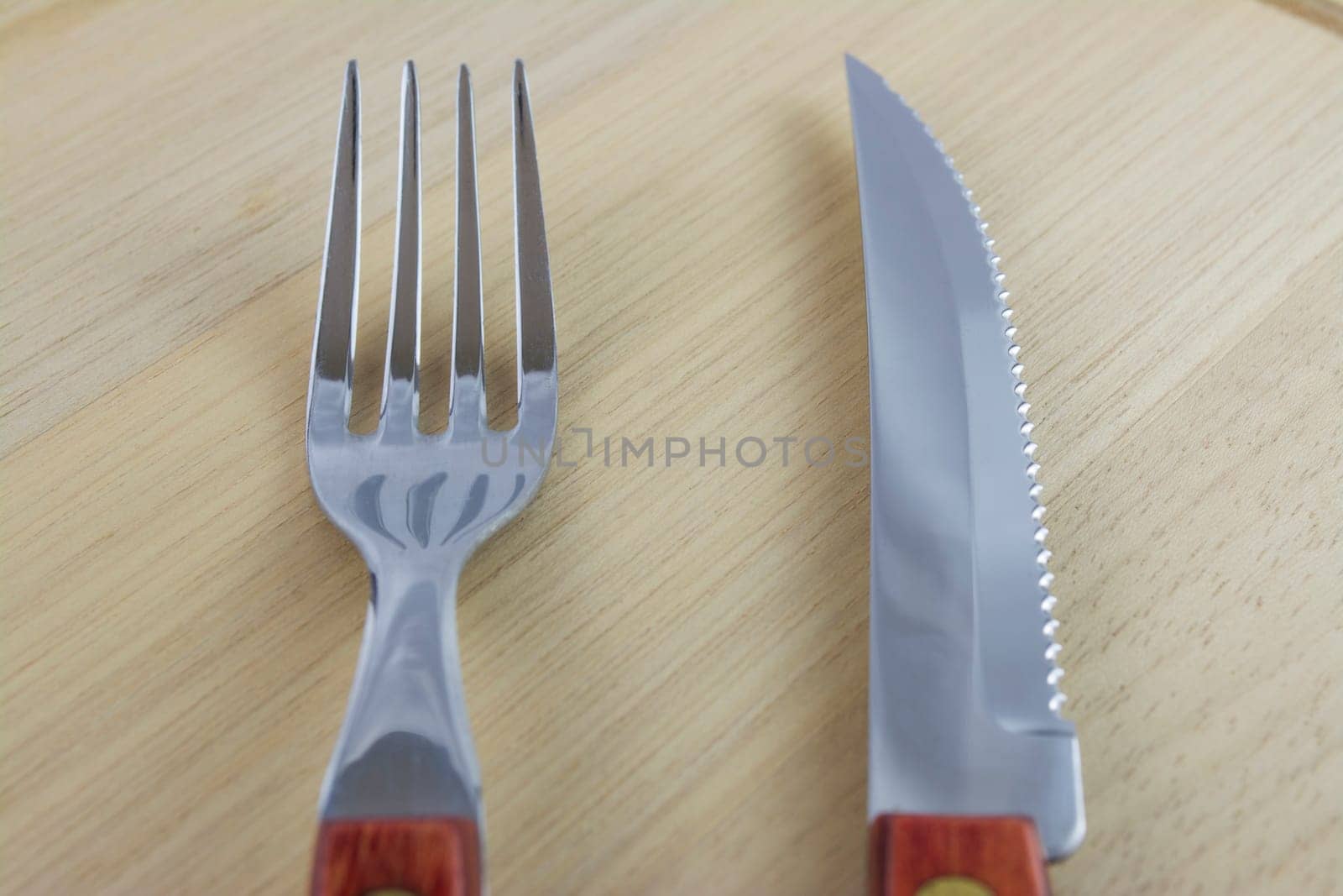 Fork and knife with red wooden handle on a plate of natural wood.