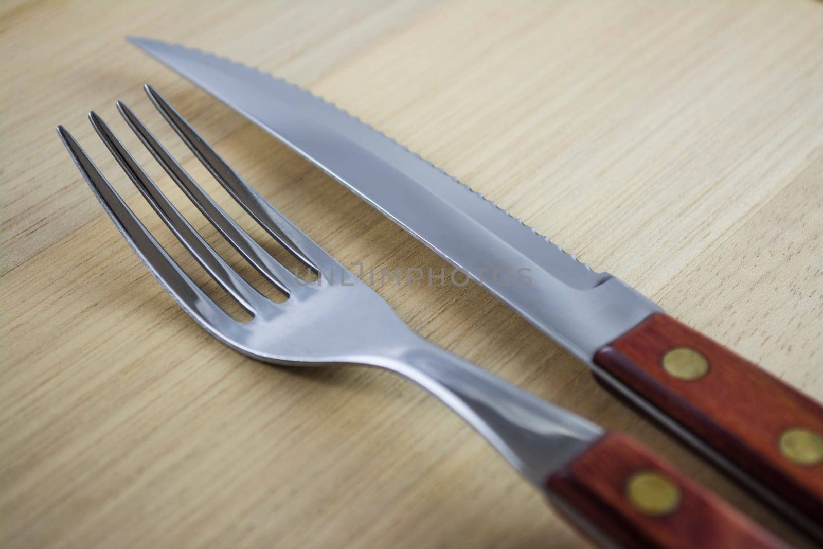 Fork and knife with red wooden handle on a plate of natural wood.